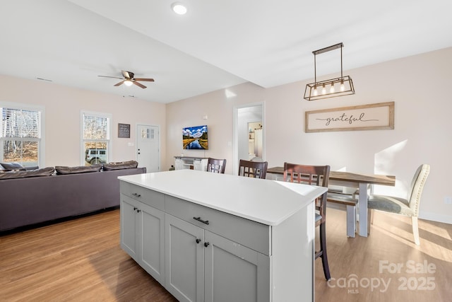 kitchen with ceiling fan, gray cabinetry, hanging light fixtures, a kitchen island, and light hardwood / wood-style flooring