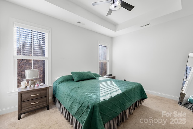 carpeted bedroom featuring ceiling fan, multiple windows, and a raised ceiling