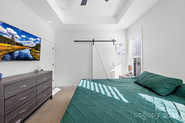 bedroom featuring ceiling fan, carpet, a barn door, and a tray ceiling