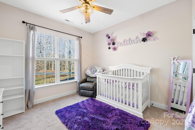 bedroom featuring ceiling fan, light colored carpet, and a crib