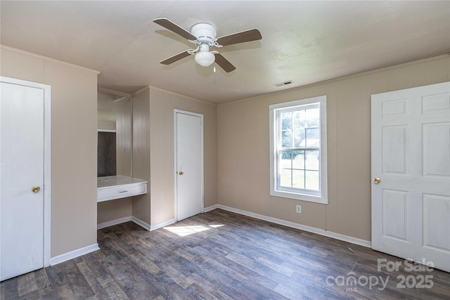 unfurnished bedroom with ornamental molding, built in desk, ceiling fan, and dark wood-type flooring