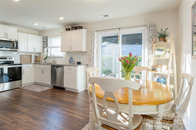 kitchen with backsplash, dark wood-type flooring, light stone countertops, stainless steel appliances, and white cabinets