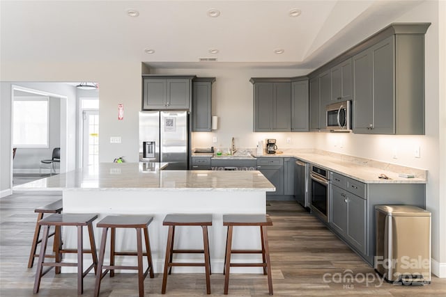 kitchen with dark hardwood / wood-style floors, appliances with stainless steel finishes, a center island with sink, and gray cabinetry