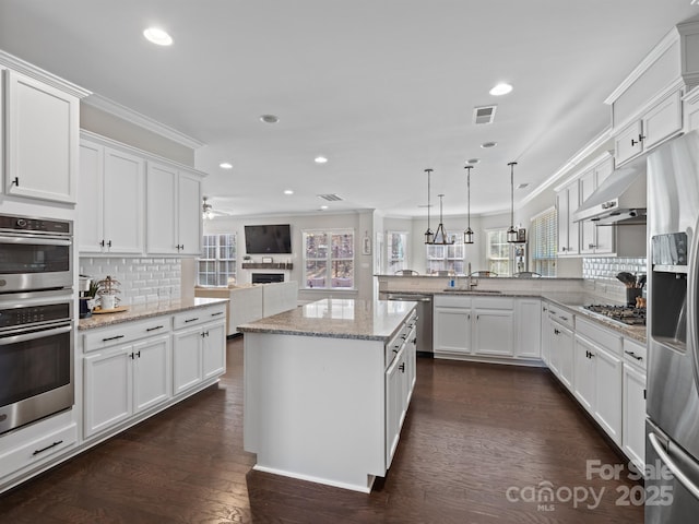 kitchen featuring appliances with stainless steel finishes, hanging light fixtures, kitchen peninsula, decorative backsplash, and white cabinetry