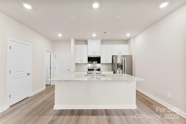 kitchen with white cabinets, an island with sink, sink, stainless steel fridge, and light stone counters