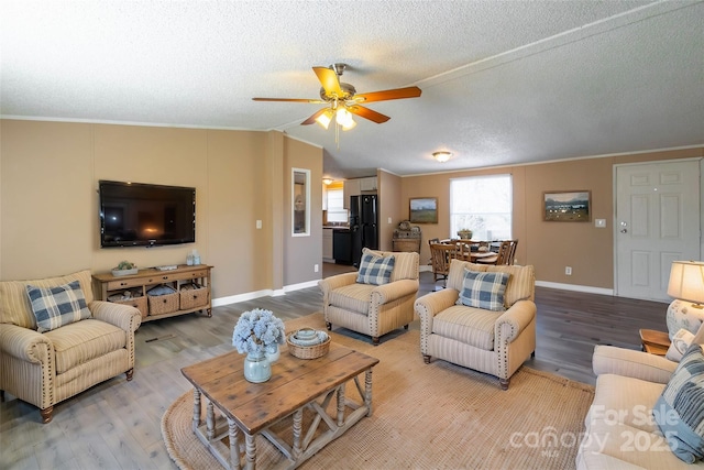 living room with a textured ceiling, ceiling fan, wood-type flooring, and ornamental molding