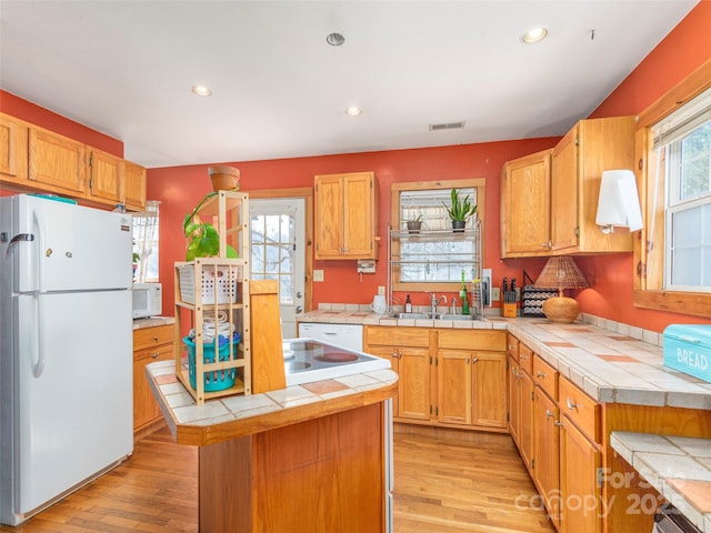 kitchen featuring tile counters, a center island, light wood-type flooring, and white appliances