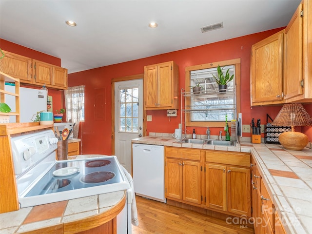 kitchen featuring light wood-type flooring, white appliances, tile counters, and sink