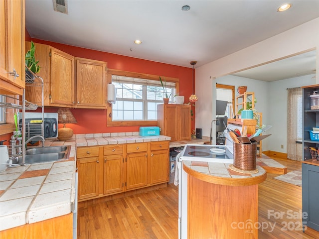 kitchen with tile countertops, decorative light fixtures, sink, and light hardwood / wood-style flooring