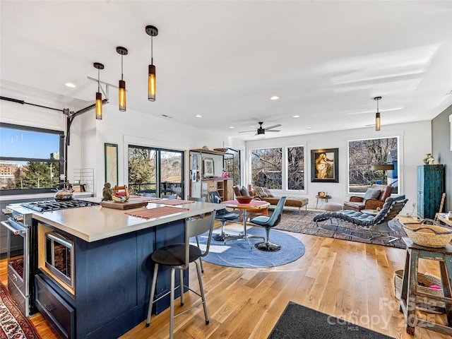 kitchen with ceiling fan, pendant lighting, light hardwood / wood-style floors, a kitchen bar, and high end stainless steel range