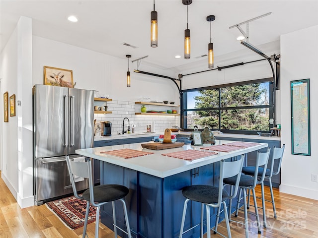 kitchen featuring a breakfast bar, sink, hanging light fixtures, stainless steel fridge, and light hardwood / wood-style floors