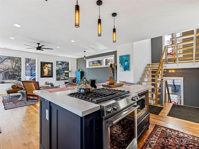 kitchen featuring ceiling fan, a center island, hanging light fixtures, light hardwood / wood-style floors, and stainless steel stove