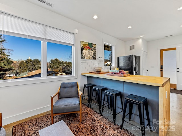 kitchen featuring wood counters, tasteful backsplash, black refrigerator with ice dispenser, kitchen peninsula, and a breakfast bar area