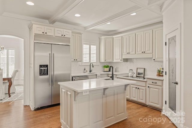 kitchen featuring a kitchen bar, stainless steel appliances, beamed ceiling, a kitchen island with sink, and light hardwood / wood-style flooring