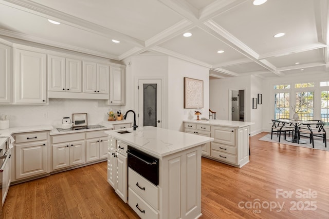 kitchen with sink, beamed ceiling, coffered ceiling, light wood-type flooring, and an island with sink