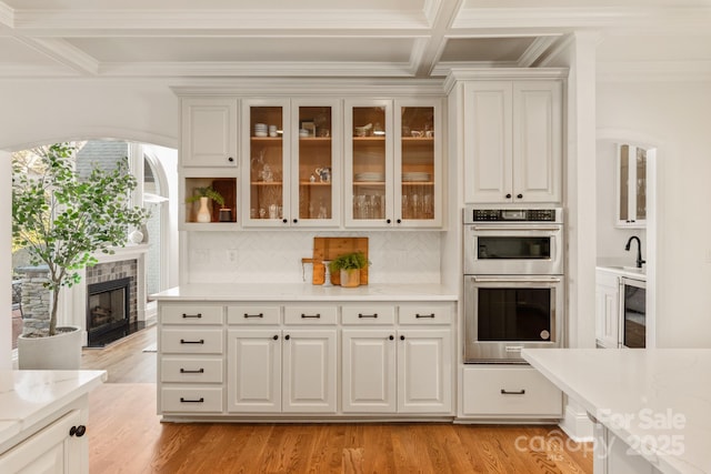 kitchen with coffered ceiling, stainless steel double oven, decorative backsplash, light stone countertops, and white cabinets