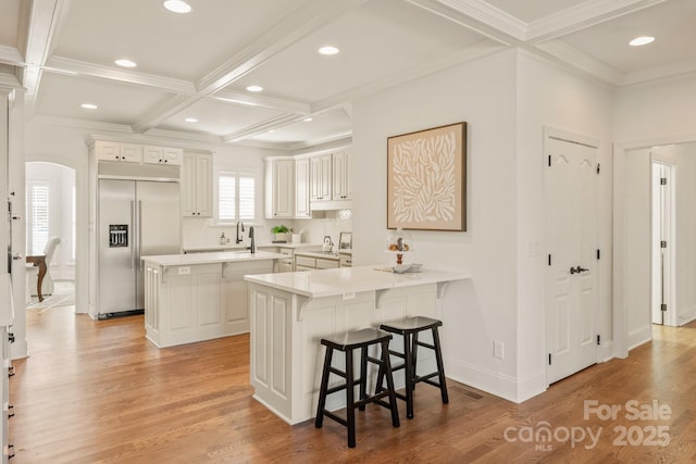 kitchen with kitchen peninsula, white cabinetry, light hardwood / wood-style flooring, a kitchen breakfast bar, and stainless steel built in refrigerator