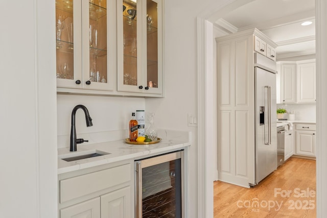 bar with light hardwood / wood-style floors, sink, crown molding, white cabinets, and beverage cooler