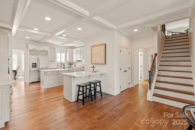 kitchen featuring light hardwood / wood-style flooring, kitchen peninsula, built in refrigerator, a kitchen breakfast bar, and white cabinets