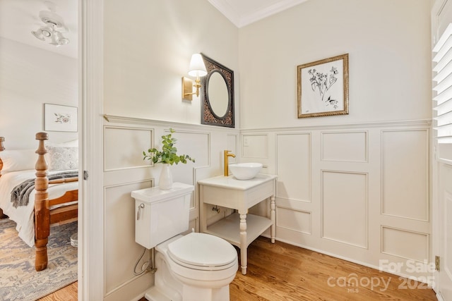 bathroom with toilet, ornamental molding, wood-type flooring, and sink