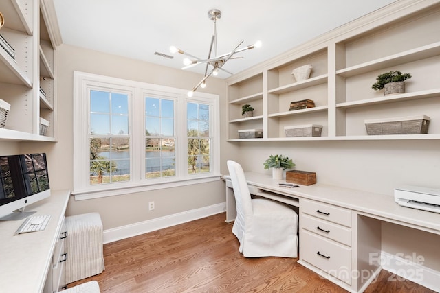 office with plenty of natural light, a chandelier, built in desk, a water view, and light hardwood / wood-style flooring