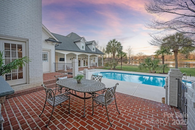 pool at dusk featuring a water view and a patio