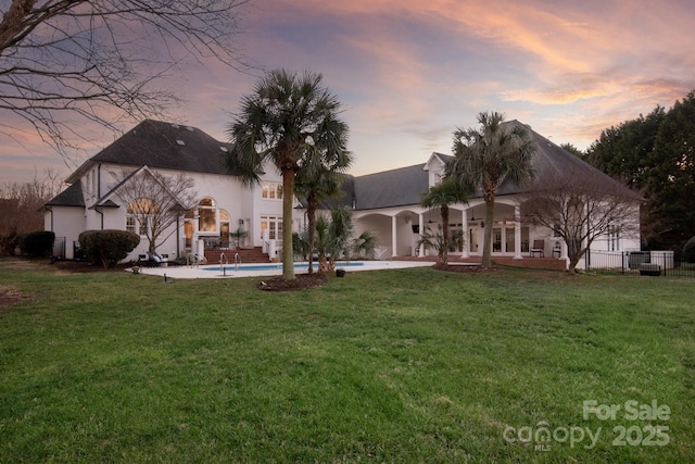 back house at dusk featuring a yard and a patio