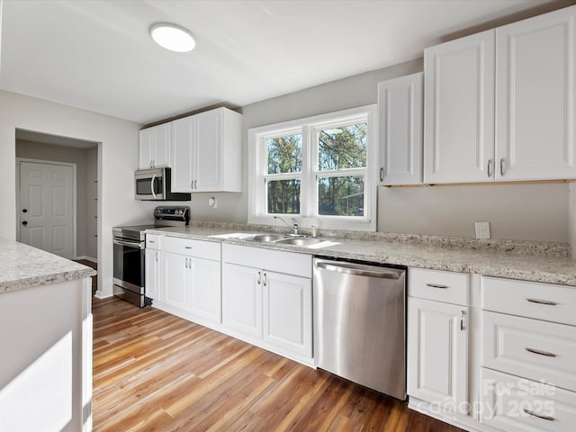 kitchen featuring sink, light stone countertops, light wood-type flooring, appliances with stainless steel finishes, and white cabinetry