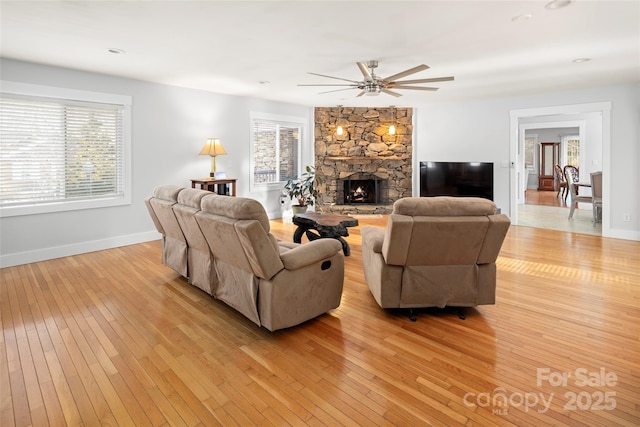 living room with ceiling fan, a stone fireplace, a wealth of natural light, and light hardwood / wood-style floors