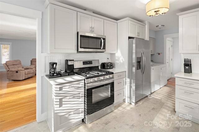 kitchen with stainless steel appliances, tasteful backsplash, white cabinets, and washer and clothes dryer