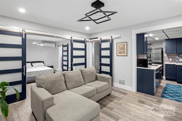 living room with a barn door, an AC wall unit, and light hardwood / wood-style floors