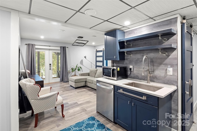 kitchen featuring blue cabinetry, sink, light wood-type flooring, stainless steel appliances, and backsplash