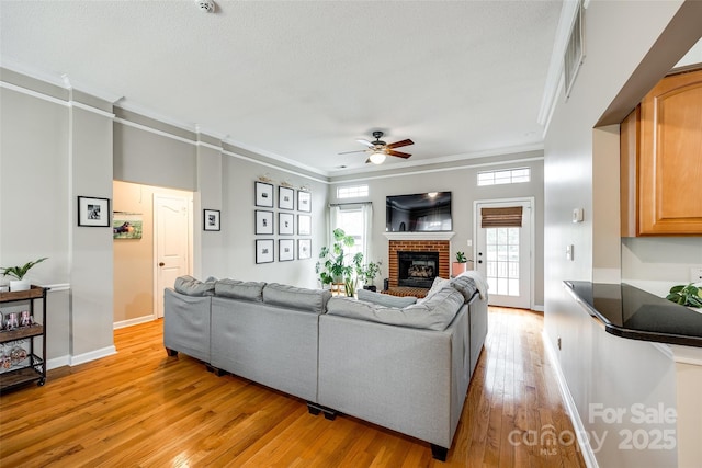 living room with a brick fireplace, ornamental molding, ceiling fan, and light wood-type flooring