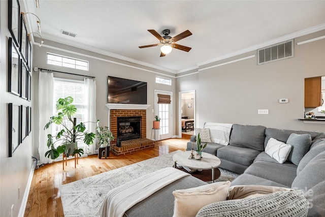 living room with a brick fireplace, crown molding, light hardwood / wood-style floors, and ceiling fan