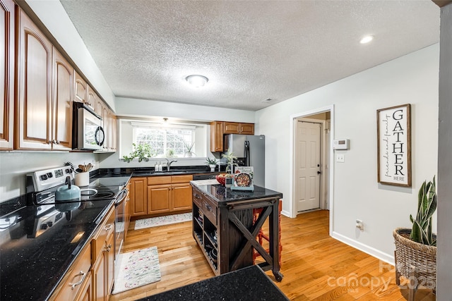 kitchen with appliances with stainless steel finishes, sink, dark stone countertops, and light wood-type flooring