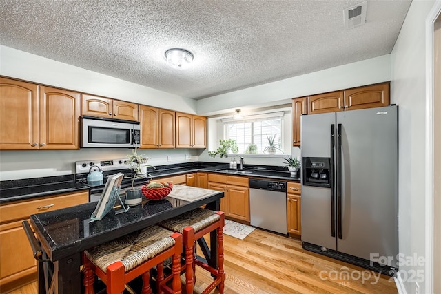 kitchen featuring appliances with stainless steel finishes, sink, a textured ceiling, and light wood-type flooring