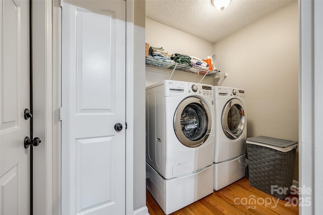 laundry area featuring a textured ceiling, washing machine and clothes dryer, and light wood-type flooring