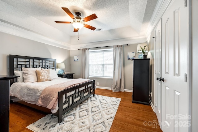 bedroom featuring hardwood / wood-style floors, a tray ceiling, a textured ceiling, and ceiling fan