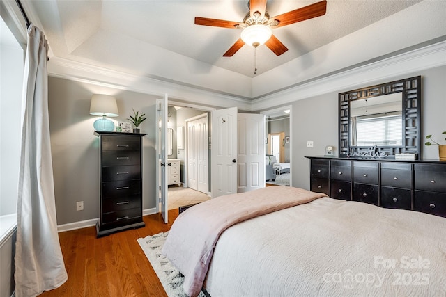 bedroom featuring a raised ceiling, wood-type flooring, ornamental molding, and ceiling fan