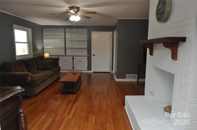 living room featuring ceiling fan, crown molding, dark wood-type flooring, and a brick fireplace