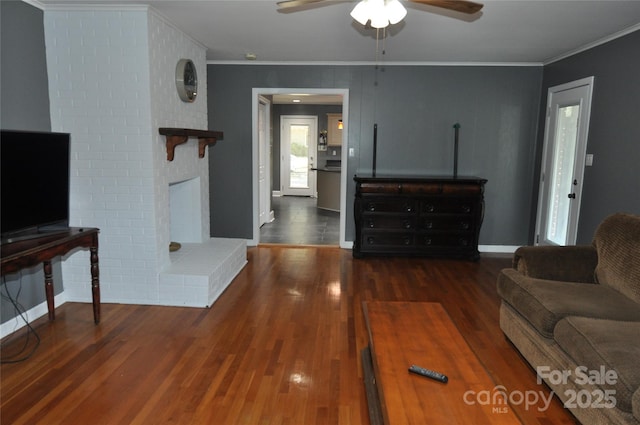 living room with dark hardwood / wood-style floors, ceiling fan, crown molding, and a fireplace