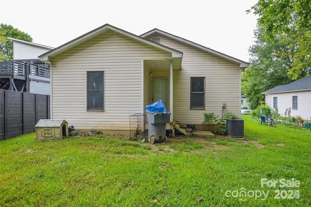 rear view of house with central air condition unit and a lawn