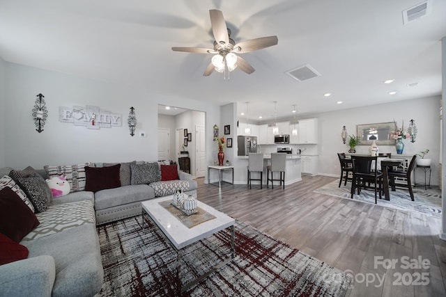 living area featuring visible vents, light wood-style floors, baseboards, ceiling fan, and recessed lighting