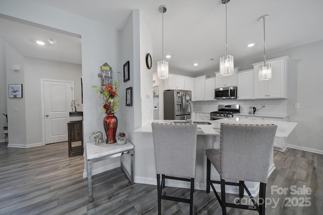 kitchen with light countertops, dark wood finished floors, stainless steel appliances, a peninsula, and tasteful backsplash