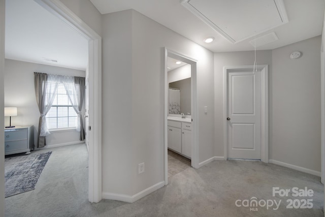 corridor featuring a sink, baseboards, light carpet, and attic access