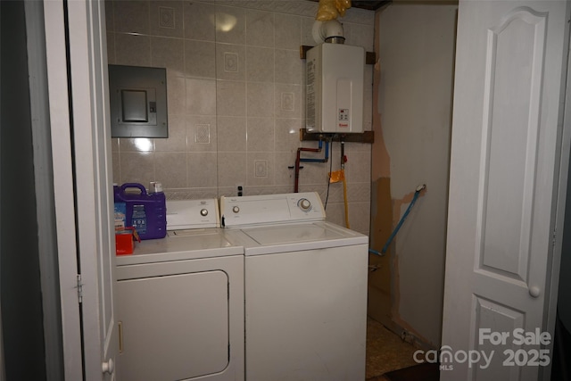 laundry area featuring tile walls, tankless water heater, washing machine and clothes dryer, and electric panel