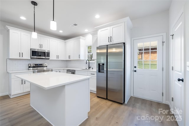 kitchen with stainless steel appliances, decorative light fixtures, white cabinetry, and sink