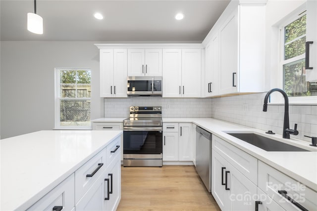 kitchen with sink, white cabinets, backsplash, pendant lighting, and appliances with stainless steel finishes