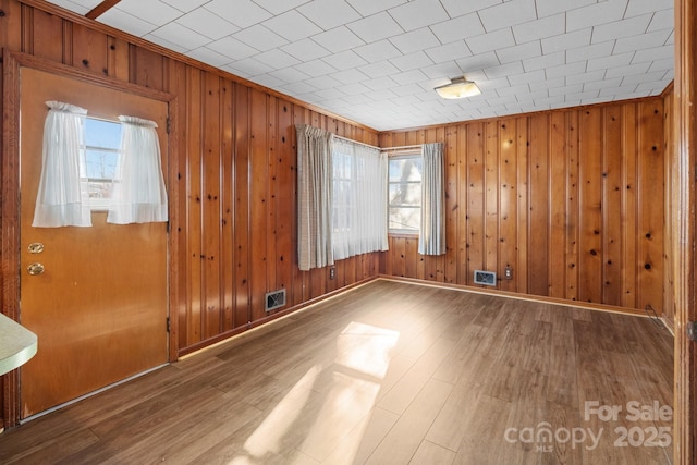 unfurnished room with wood-type flooring, wooden walls, and a wealth of natural light