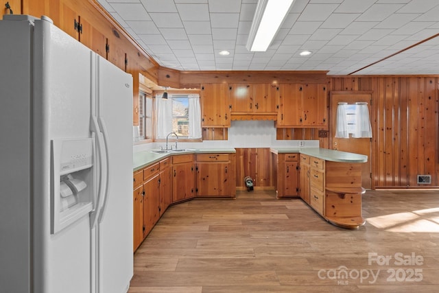 kitchen featuring sink, light hardwood / wood-style flooring, white refrigerator with ice dispenser, and wood walls